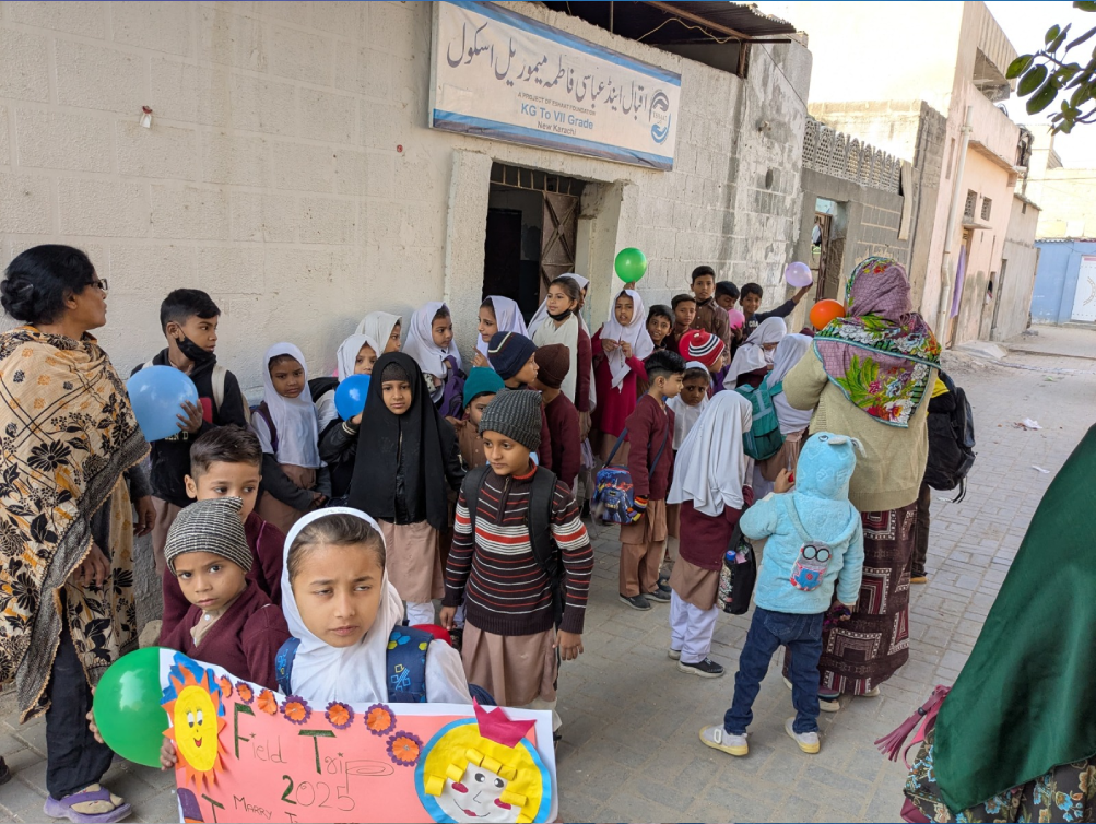 Eshaat school students are standing outside the school to go on a field trip.
